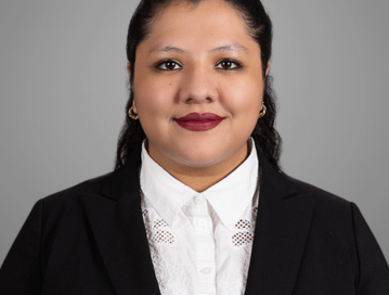 Portrait of Dolores Jimenez-Cruz, an immigration legal assistant based in Winston-Salem, NC. She is wearing a professional black blazer over a white blouse with lace detailing. Dolores has dark hair styled back and is smiling confidently against a plain gray background.