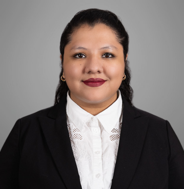 Portrait of Dolores Jimenez-Cruz, an immigration legal assistant based in Winston-Salem, NC. She is wearing a professional black blazer over a white blouse with lace detailing. Dolores has dark hair styled back and is smiling confidently against a plain gray background.